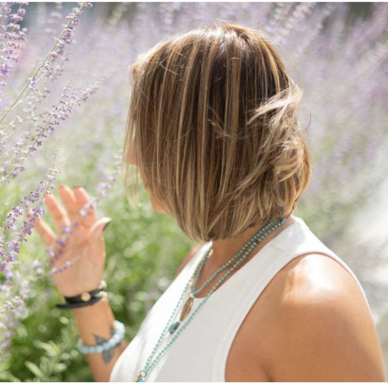 Erika seen from behind, reaching out to touch tall lavender in bright sunlight.