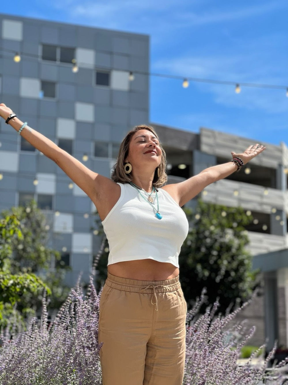 Erika outdoors with her arms open wide and her face turned to the sun, standing among lavender.